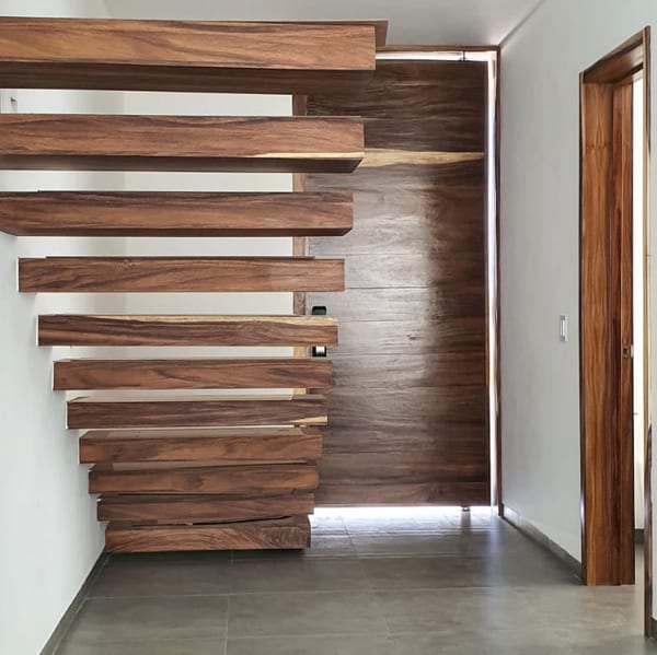 Escalera flotante de madera, con los peldaños empotrados en el muro y una puerta de madera al fondo.