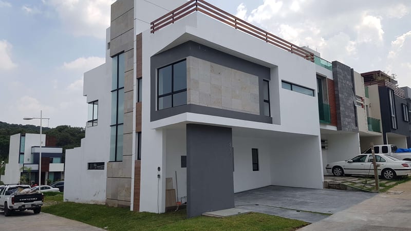 Exterior de vivienda contemporánea de dos niveles en calle residencial, con volumen blanco y cochera.