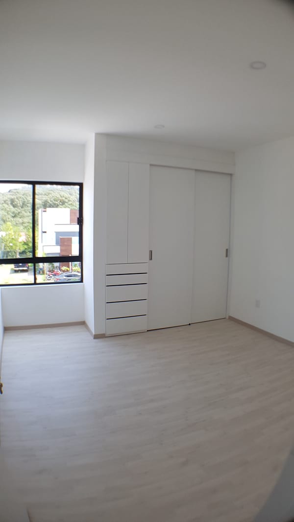 Habitación vacía con ventana al jardín, piso de duela y puertas de clóset.