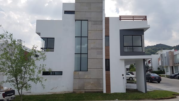 Fachada de la vivienda terminada, con volumen blanco, cantera y ventanales oscuros.