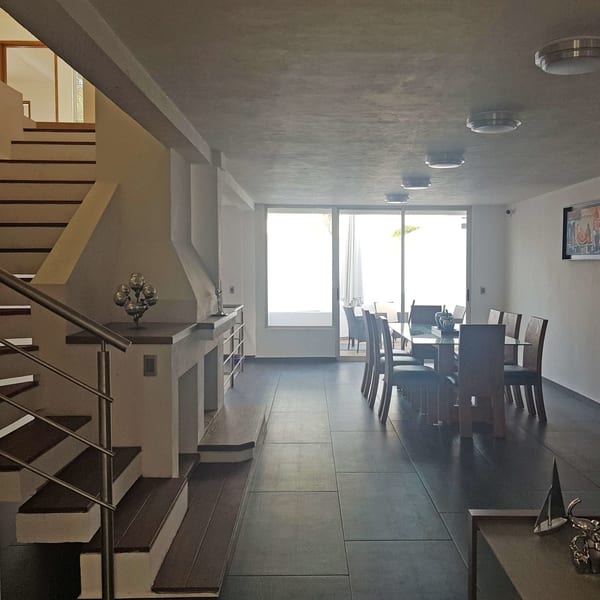 Estancia con la escalera a un costado, comedor de madera y ventanal corredizo al patio.