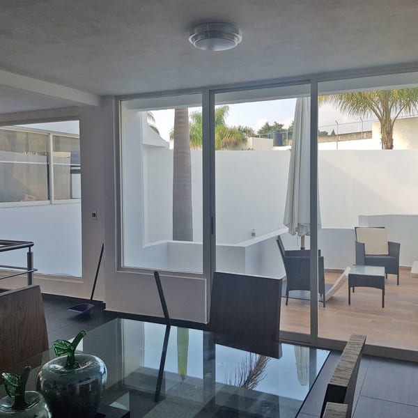 Patio visto a través del ventanal corredizo, con mobiliario de exterior y una palmera.