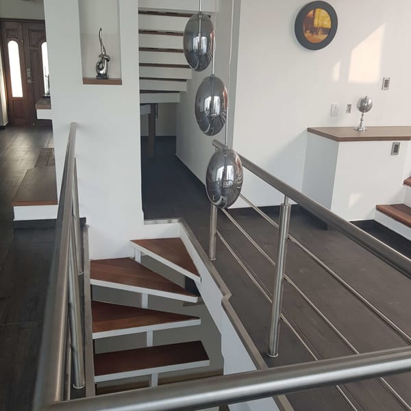 Escalera con peldaños de madera y barandal de acero, con esferas decorativas en el muro.