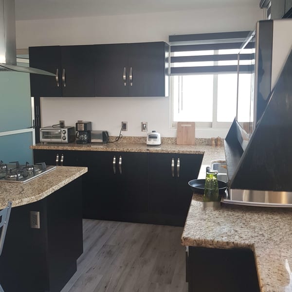 Cocina con alacenas oscuras, cubierta de granito y persiana en la ventana.
