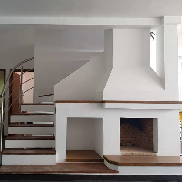 Chimenea de obra blanca junto a la escalera de madera con barandal de acero.